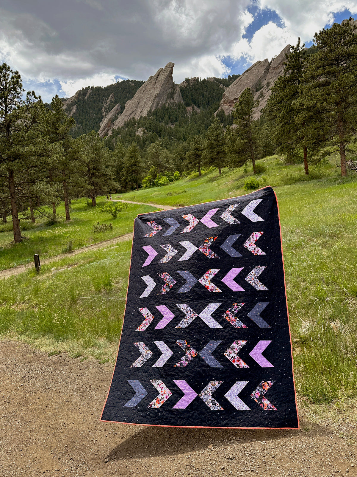 The Due Pinoli Midnight on the 707 quilt pattern featuring the Art Gallery Fabrics Eerie collection by Katarina Roccella blows gently in the breeze on a hiking path in front of the Flatirons mountains in Boulder Colorado