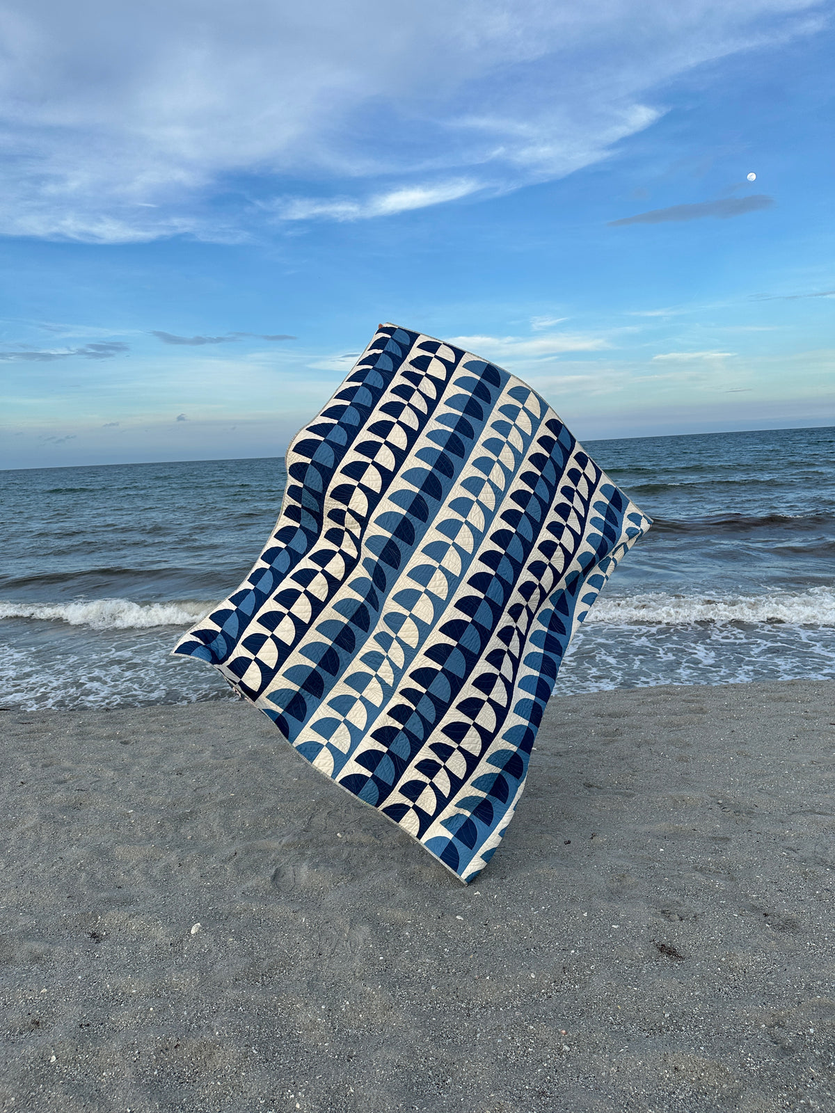 The Due Pinoli With You quilt blowing in the wind in the evening light on a beach in south Florida with gentle waves in the background